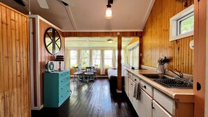 A kitchen with wooden walls, a dining area with chairs, a sink, and a window. - Waterfront Cabin w/ Dock Access, Fishing & Kayaks
Beach Retreat - Cabin 3 (South Haven)
