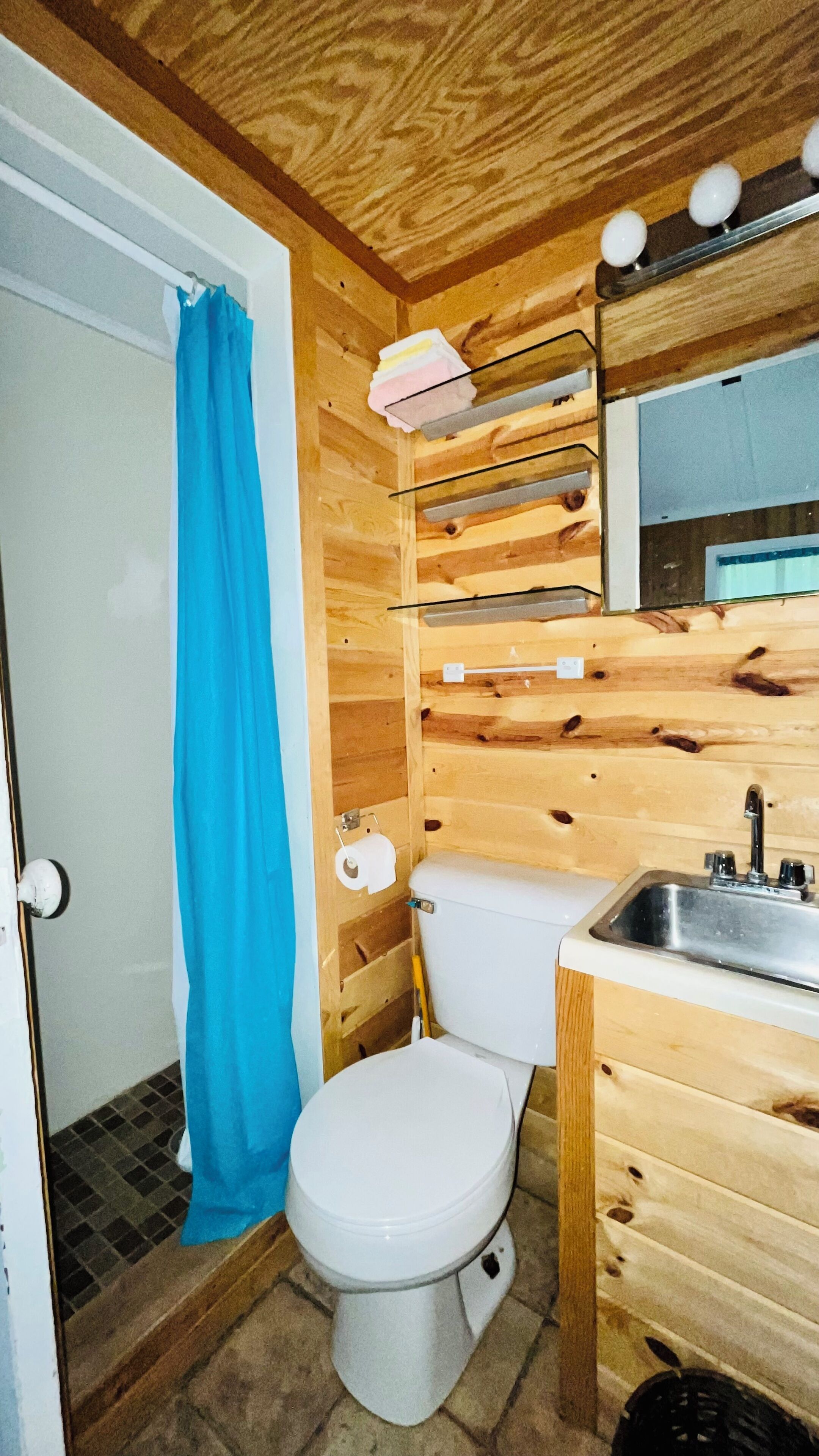 A compact wooden bathroom with a toilet, sink, and shower area.