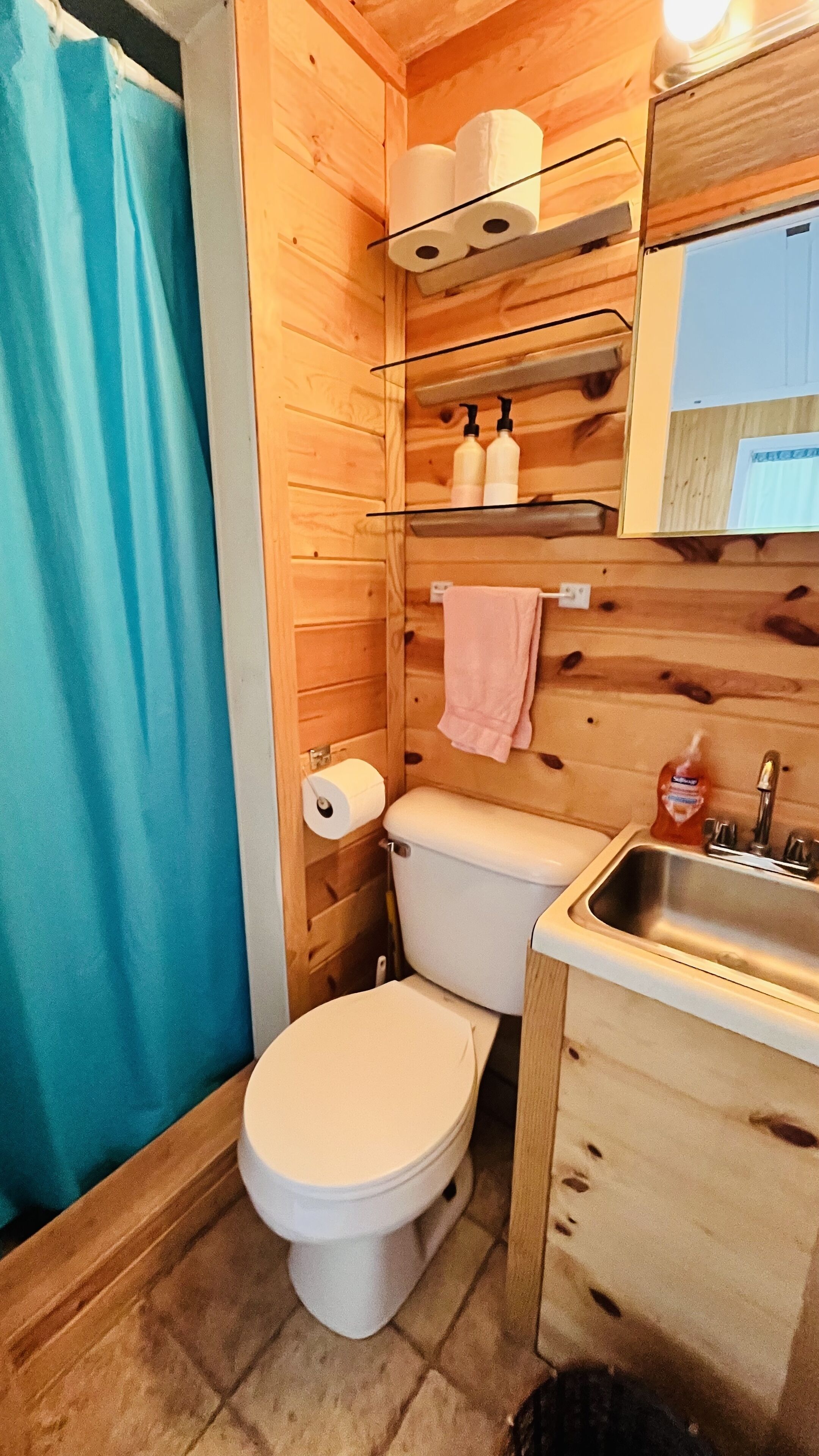 Et badeværelse i træ med toilet, vask og hylder med toiletartikler.