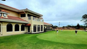 Un bâtiment doté d’un toit plat et d’un balcon, situé à côté d’une pelouse bien entretenue, agrémentée de balises de parcours de golf.