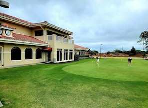A building with a flat roof and a balcony, adjacent to a well-maintained lawn with golf course markers.