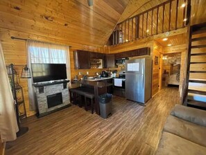 Cozy cabin-style room with a lofted sleeping area, flat-screen TV, and kitchenette.