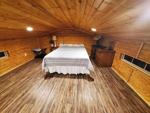 Cozy cabin with a central bed, wooden dresser, and table with a lamp.