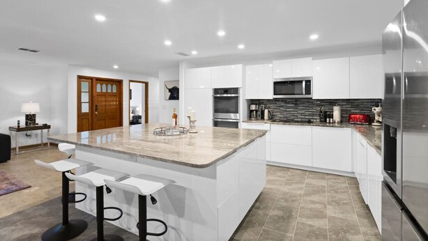 A modern kitchen with white cabinetry, a central island with bar stools, stainless steel appliances, and a tiled backsplash. - Luxury Villa with Heated Saltwater Pool & Spa, Mini Golf, BBQ, 5 Mins to Beach (Largo)
