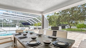 A dining area with a table set for four, a pool, and a covered outdoor seating area. - Luxury Villa with Heated Saltwater Pool & Spa, Mini Golf, BBQ, 5 Mins to Beach (Largo)