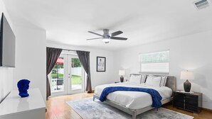 A modern bedroom with a bed, bedside tables, a ceiling fan, and a view of the outdoors. - Luxury Villa with Heated Saltwater Pool & Spa, Mini Golf, BBQ, 5 Mins to Beach (Largo)