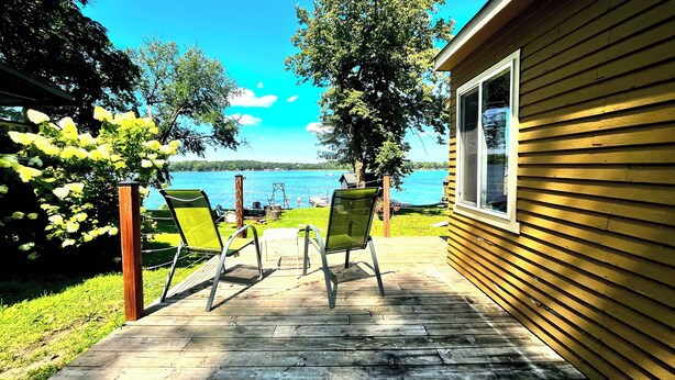 A wooden deck with two chairs facing a lake, a small wooden building, and a clear sky. - Cozy Lakefront Cabin, Dock, Fire Pit & Sunset Views
Tiny Barn - Cabin 4 (South Haven)