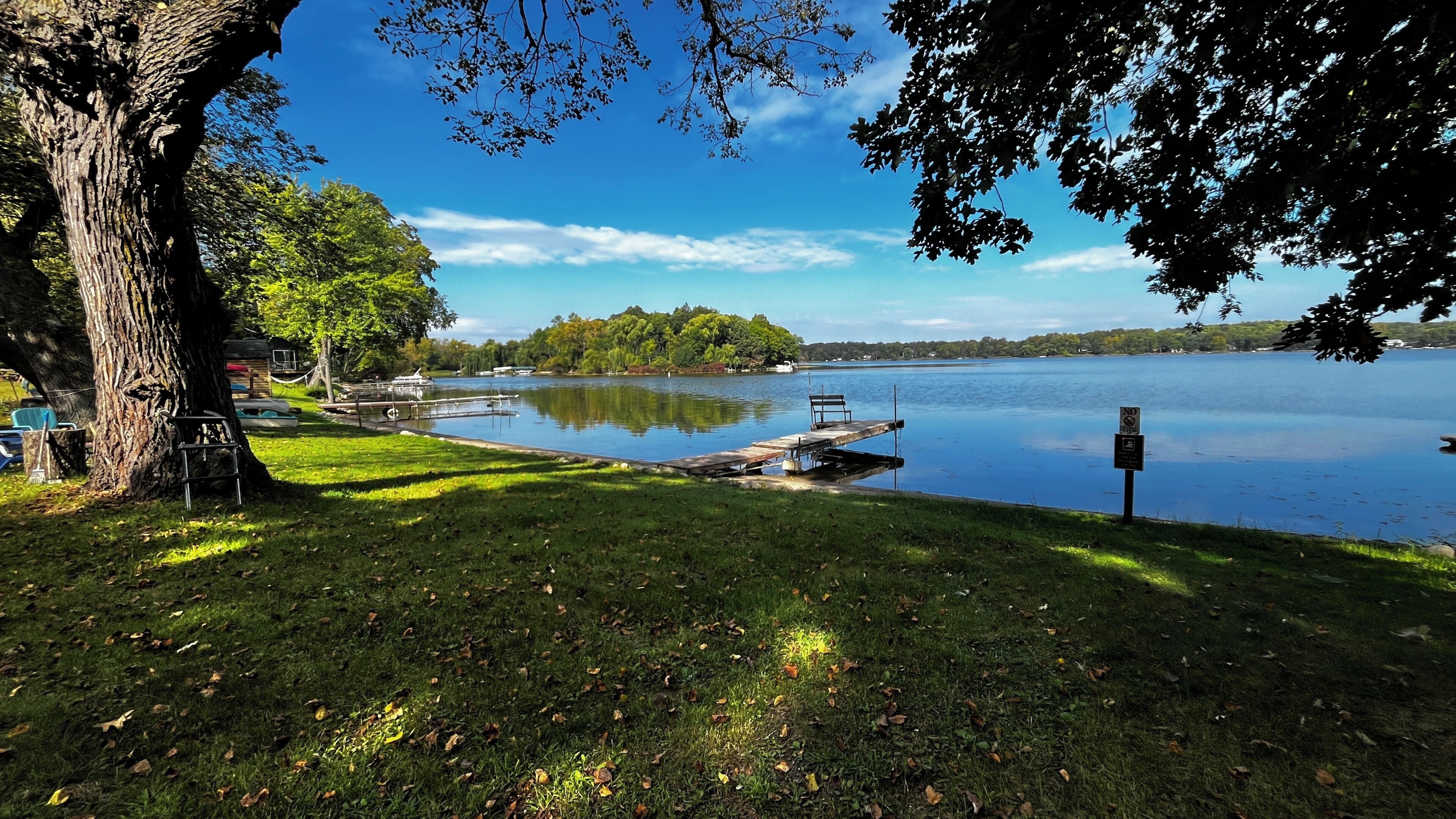 A lakeside park with a dock, benches, and a sign indicating no swimming.
