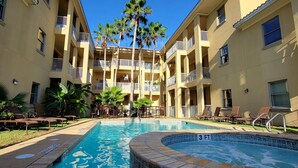 Ein Hotel mit einem zentral gelegenen Schwimmbad, mehreren Balkonen und Palmen.