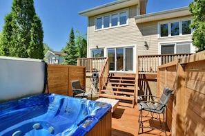 Un patio trasero con jacuzzi, terraza de madera y una casa de dos pisos.