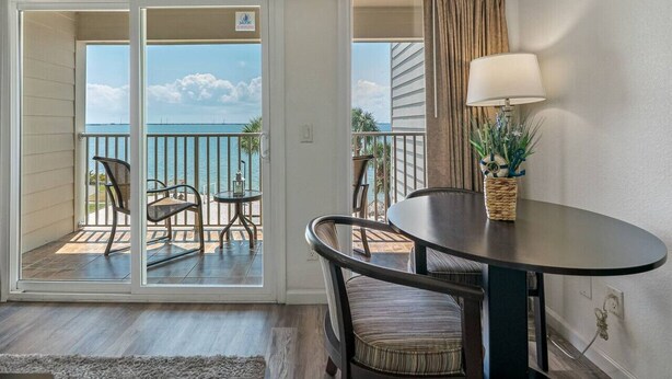 A room with a balcony, a table with chairs, a lamp, and a plant. - Wake up to Ocean Views from your private balcony! (Tampa)