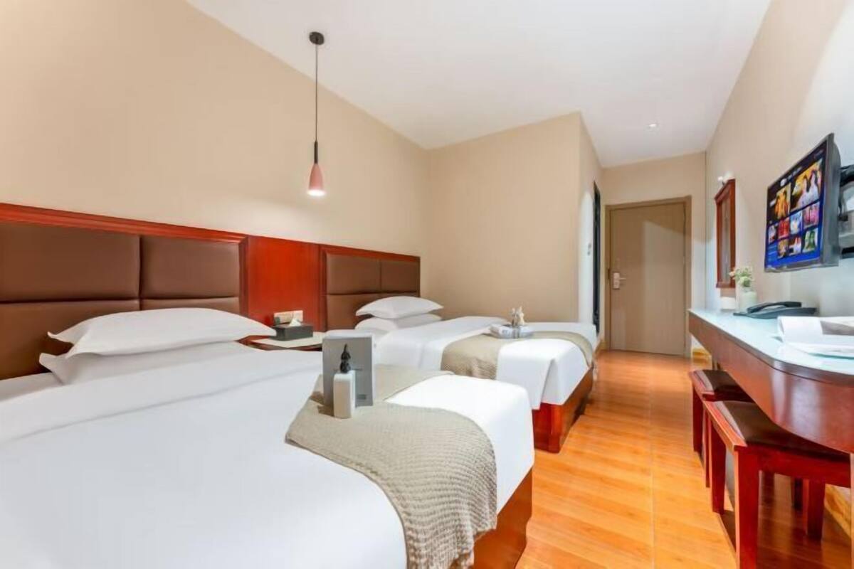 Een hotelkamer met drie bedden, een houten hoofdeinde, een bureau en een televisie.