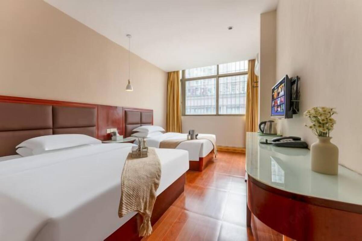 Een hotelkamer met twee bedden, een televisie, een bureau en een raam met gordijnen.