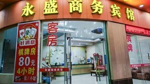 Een hotelentree met een bord waarop 'Water Mansion Business Hotel' staat en een rood bord dat een verblijf van 4 uur voor 80 yuan adverteert.