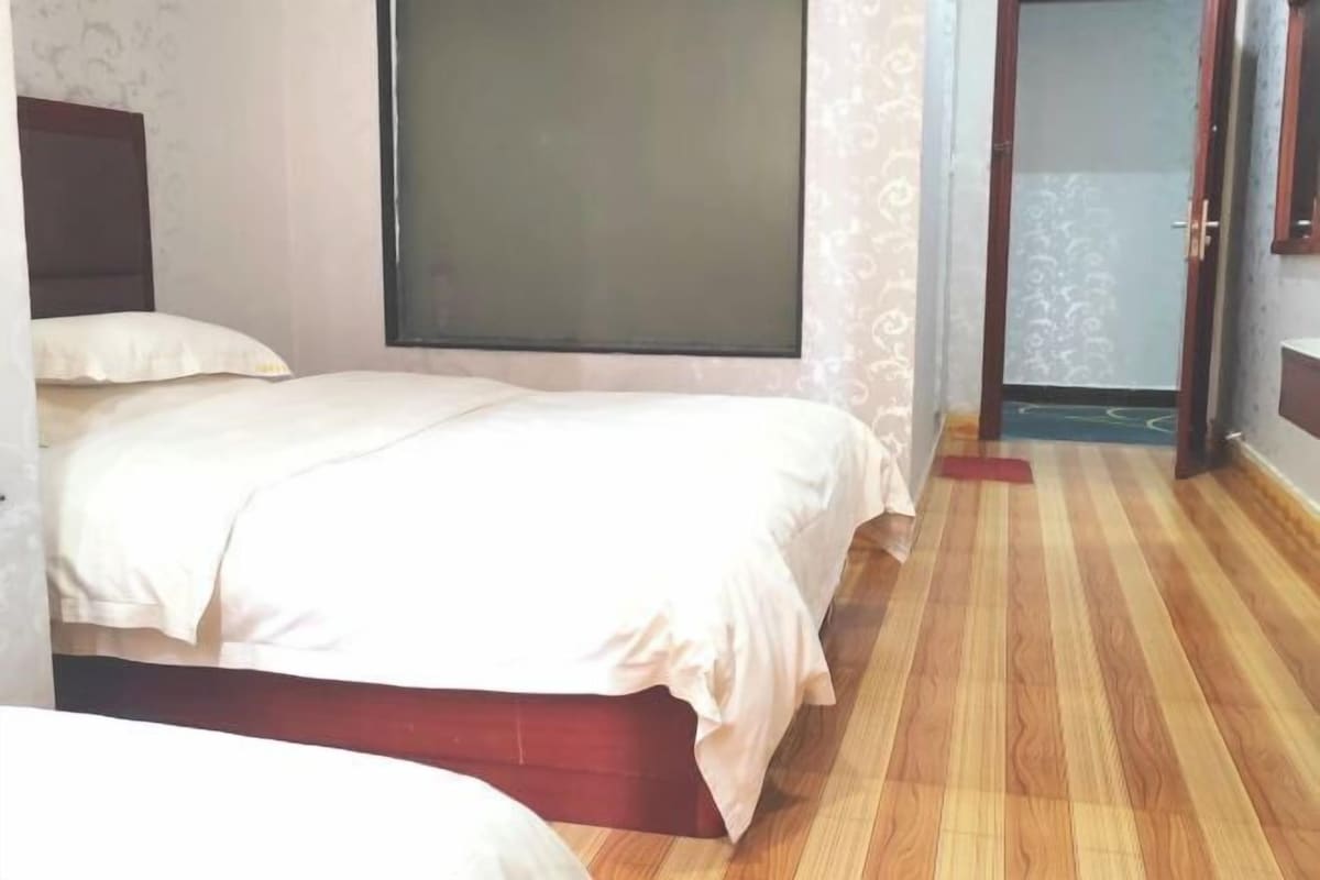 A bedroom with a bed, a wooden floor, and a door leading to another room.