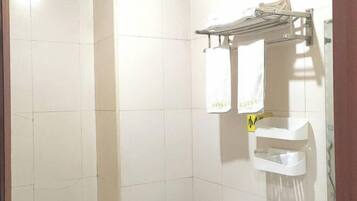 A bathroom with white tiled walls, a towel rack with two white towels, and a small sink with a trash bin.