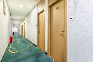 Een hotelgang met deuren aan de rechterkant, een vloerbedekking en een patroon op de muur links.
