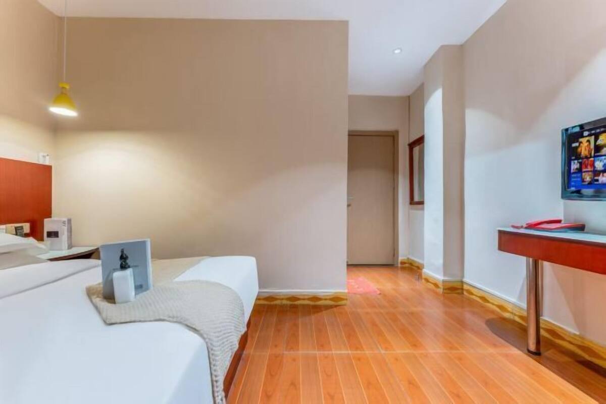 Een hotelkamer met een bed, een bureau, een televisie en een deur naar een andere kamer.