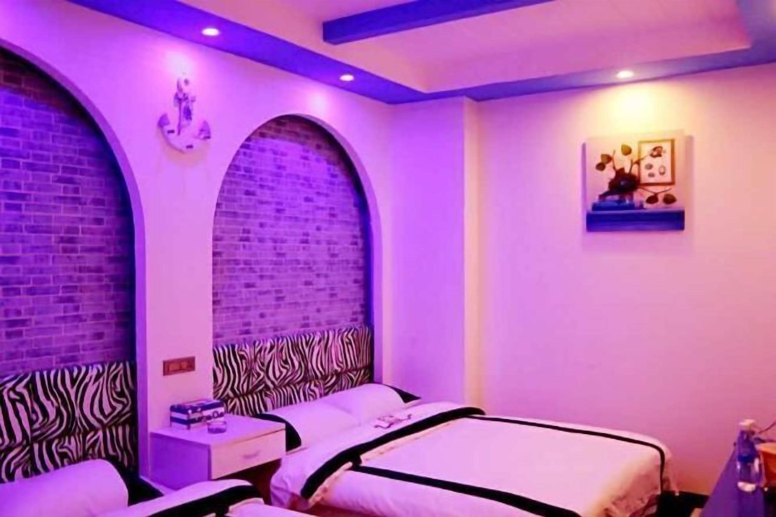 A room with two beds, zebra-patterned headboards, brick walls, and a small shelf with decorative items.