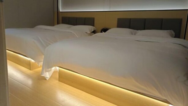 Quarto de hotel com duas camas, piso de madeira e design moderno para a cabeceira.