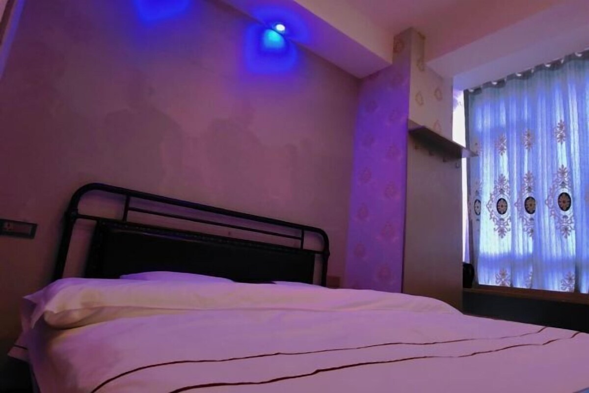 A bedroom with a single bed, a window with patterned curtains, and a ceiling light.