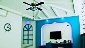Quarto com ventilador de teto, escrivaninha com televisão de tela plana e janela com moldura decorativa.