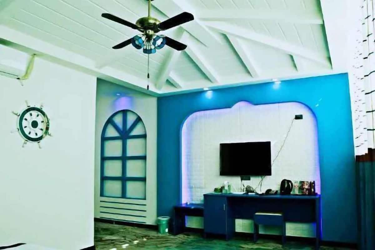 Ein Zimmer mit Deckenventilator, Schreibtisch mit Flachbildfernseher und Fenster mit Zierrahmen.
