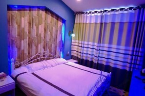 A bedroom with a bed, a nightstand, a wall with a wooden panel design, and a window with curtains.