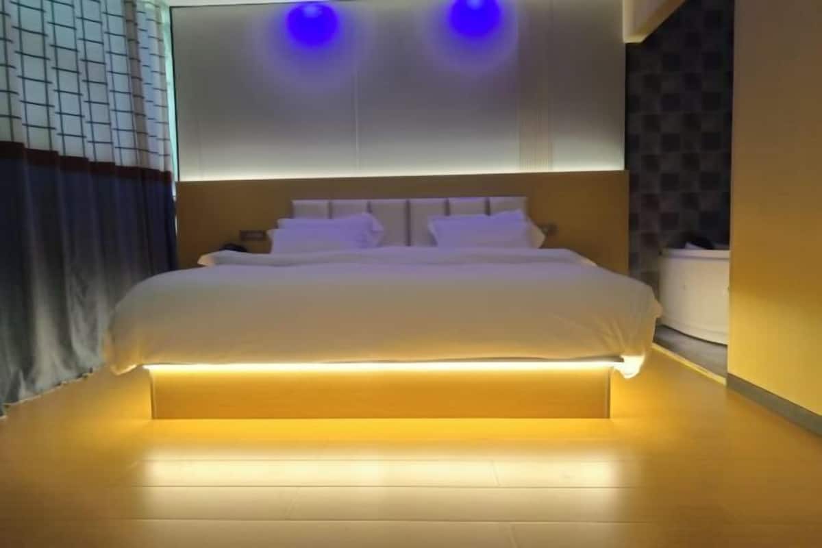 Ein modernes Hotelzimmer mit einem großen Bett, einem einlichteten Kopfteil und einer Wandleuchte.