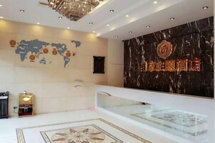 Zona de recepción de un hotel con un mapa mundial, un mostrador de recepción y una pared de mármol con la señalización del hotel.