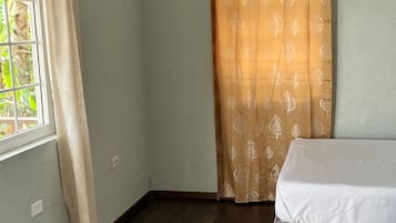 Une pièce avec une fenêtre, un rideau, un lit et un appareil de climatisation.