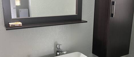Un baño con un lavamanos blanco, un mueble de madera oscura y un espejo sobre el lavamanos.