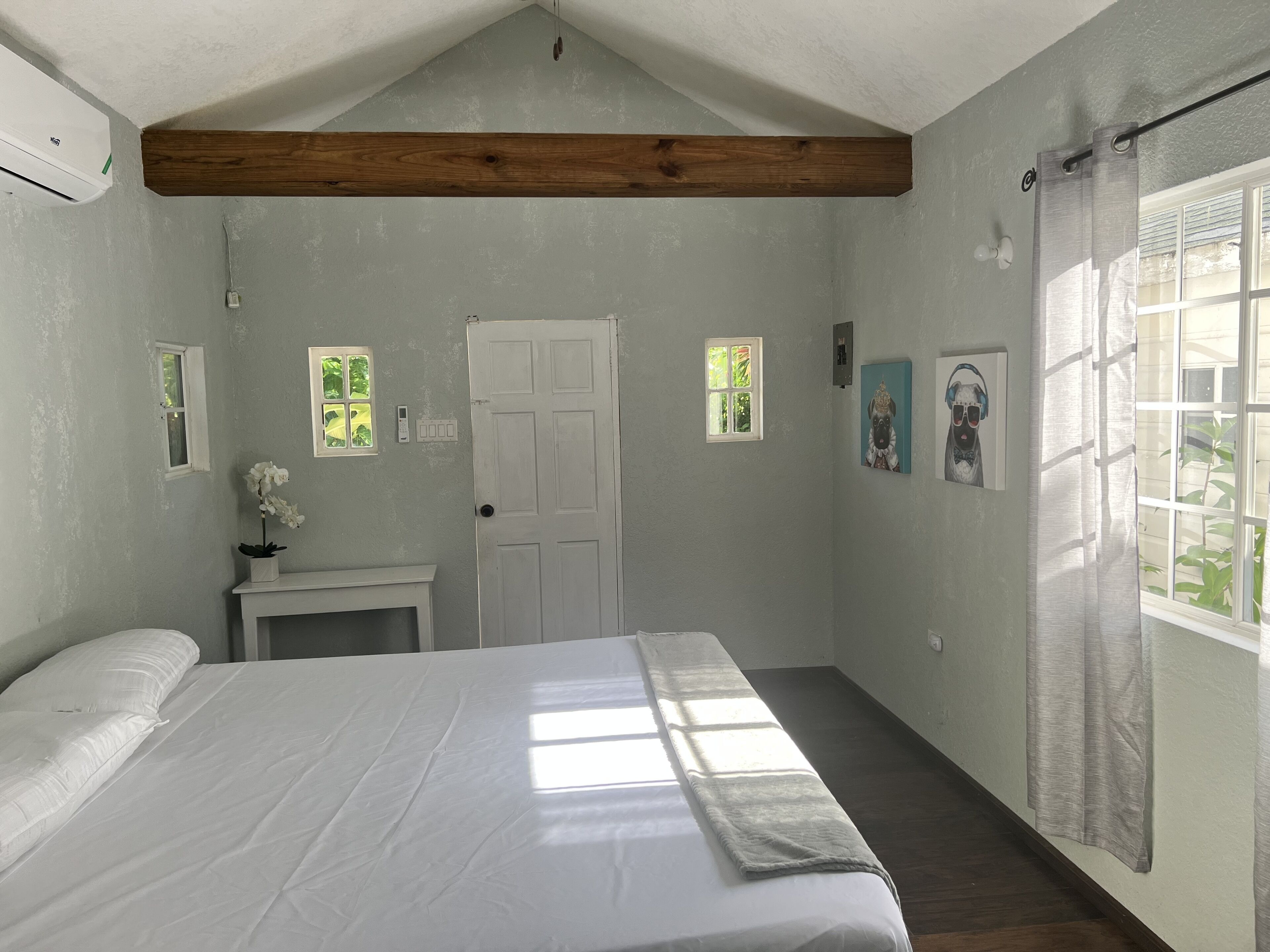 Quarto com uma cama, uma mesinha com uma planta em vaso, uma porta e uma janela com cortina.