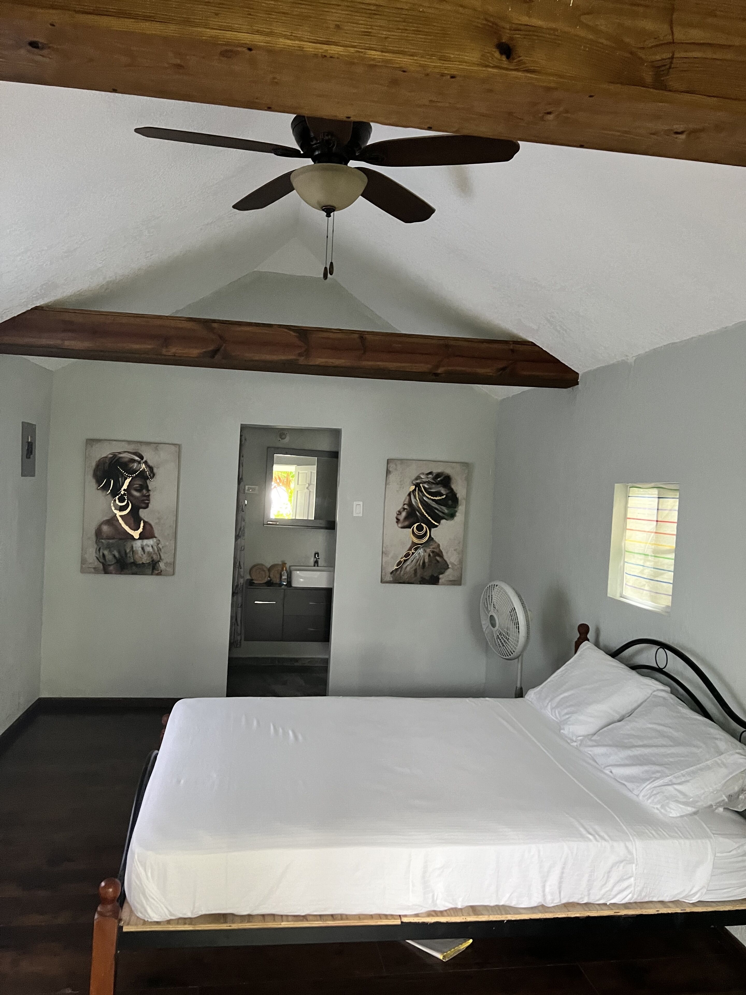 A bedroom with a bed, ceiling fan, and two wall-mounted fans. There are two doors leading to other rooms.
