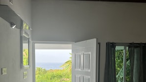 A room with a bed, a door leading to a balcony, a window with curtains, and a view of the ocean. - Jamaica Colors Eco-Retreat Hotel and Spa (Rural Hill)