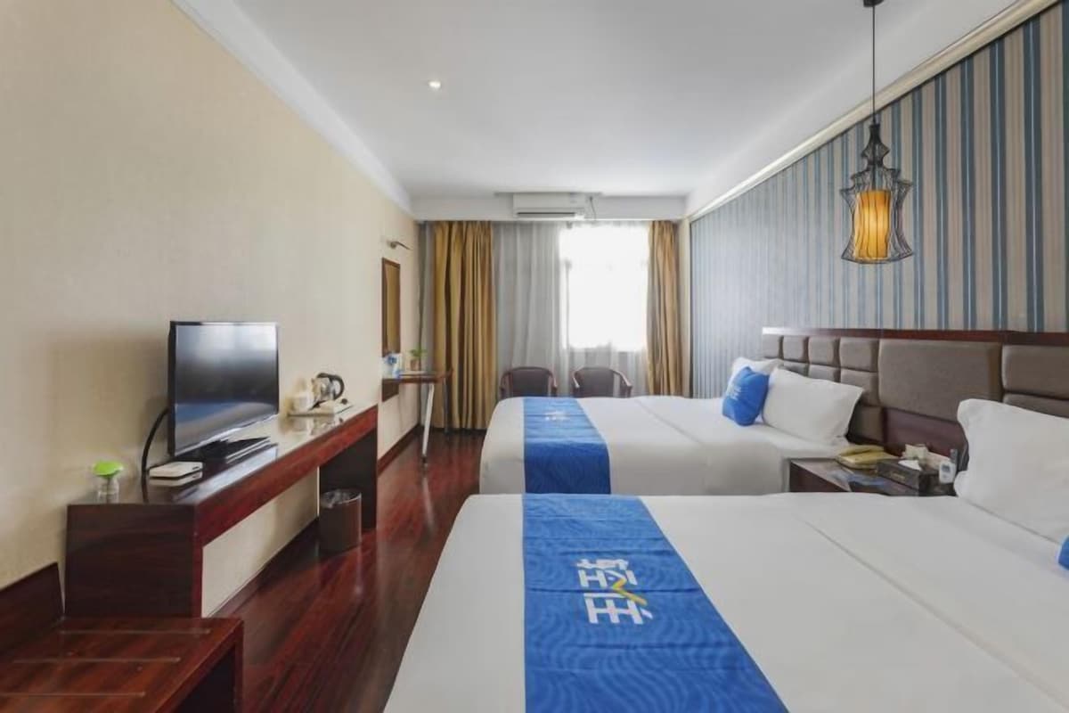Ein Hotelzimmer mit zwei Betten, einem Fernseher, einem Schreibtisch und einem Fenster mit Vorhängen.