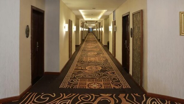 Ein Hotelgang mit Teppichmuster, Türen und Wandleuchten.