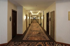 Un pasillo de hotel con alfombra estampada, puertas y luces en la pared.