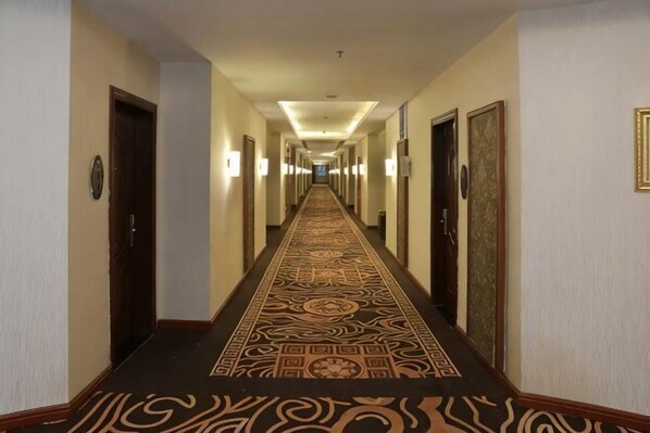 Un pasillo de hotel con alfombra estampada, puertas y luces en la pared.