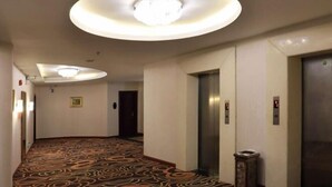 Ein Hotelkorridor mit gemustertem Teppich, einer runden Leuchte und einem Aufzug.