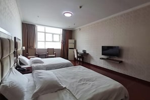 Ein Hotelzimmer mit zwei Betten, einem Schreibtisch, einem Stuhl, einem Fernseher und einem Fenster mit Vorhängen.