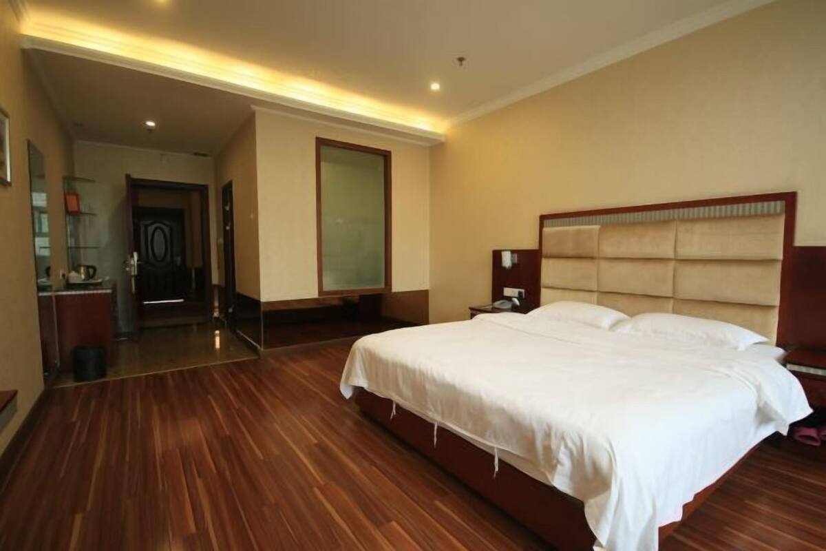 Una habitación de hotel con una cama grande, suelo de madera, una mesita de noche y un espejo.