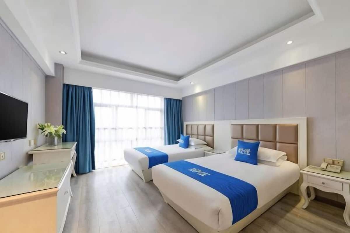 Habitación de hotel con dos camas, televisión, escritorio y ventana con cortinas.