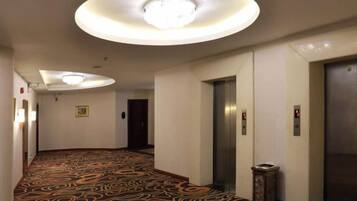 A hotel corridor with a patterned carpet, a circular light fixture, and an elevator.