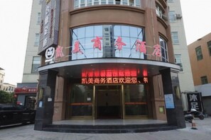 L’entrée d’un hôtel, avec une façade incurvée, de grandes fenêtres en verre et une enseigne bien visible, ornée de caractères chinois.