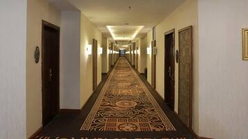 Un pasillo de hotel con alfombra estampada, puertas a ambos lados y luces fijadas a la pared.