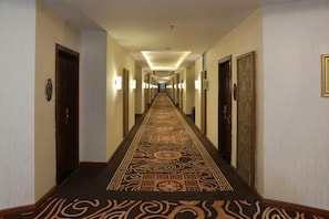 Ein Hotelkorridor mit gemustertem Teppich, Türen auf beiden Seiten und Wandleuchten.