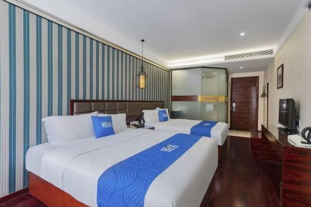 Ein Hotelzimmer mit zwei Betten, einem Holzkopfteil, einem Fernseher und einer Glaskabine.