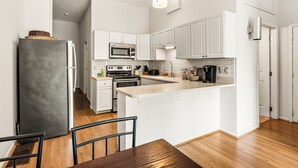 Eine moderne Küche mit weißen Schränken, einer zentralen Kochinsel, Edelstahlgeräten und einem Essbereich mit Holztisch und Stühlen.