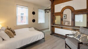 Un dormitorio con cama, una silla, un armario de madera y un espejo.